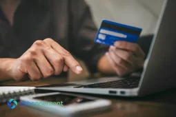 Persona che inserisce dati su un laptop mentre tiene una carta di pagamento, simbolo dei rischi e delle attenzioni da avere quando si decide di comprare online.