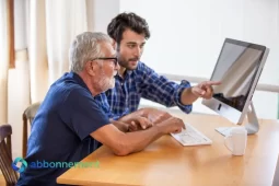 Due persone davanti a un computer mentre un giovane aiuta un uomo anziano a superare il Digital Divide.