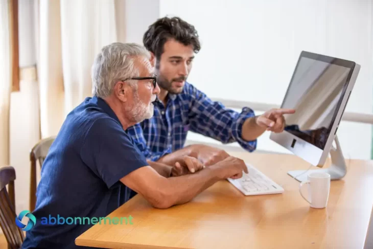 Due persone davanti a un computer mentre un giovane aiuta un uomo anziano a superare il Digital Divide.