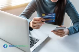 Donna che controlla il Punteggio di Credito online usando carta e smartphone davanti al laptop.