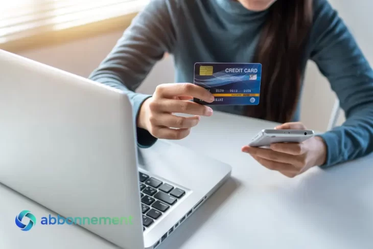 Donna che controlla il Punteggio di Credito online usando carta e smartphone davanti al laptop.