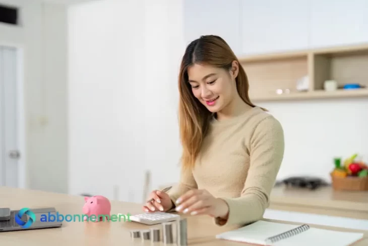 Mujer sonriendo mientras usa una calculadora y organiza monedas, enfocada en sus metas financieras.