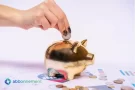 Mano poniendo una moneda en una alcancía dorada, simbolizando la duda sobre si un Plazo Fijo Conviene para resguardar el dinero.