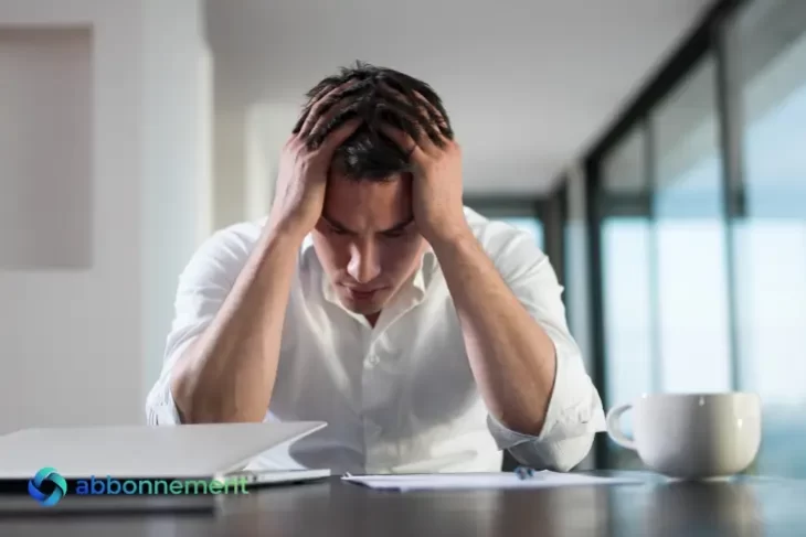 Uomo seduto alla scrivania con le mani tra i capelli mentre guarda dei documenti, stressato dalle Spese Impreviste.
