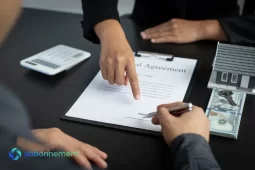 Persona firmando un contrato y revisando condiciones de préstamos ANSES para AUH con calculadora y dinero sobre la mesa.