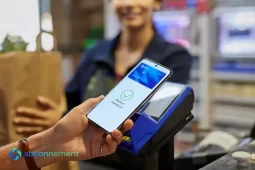 Pix en Argentina, una persona paga con el celular en una terminal de cobro, con “Payment Complete” en la pantalla, y una cajera sostiene una bolsa de compra al fondo.