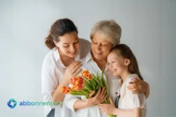 Donna anziana abbracciata da figlia e nipote con fiori, festa della mamma