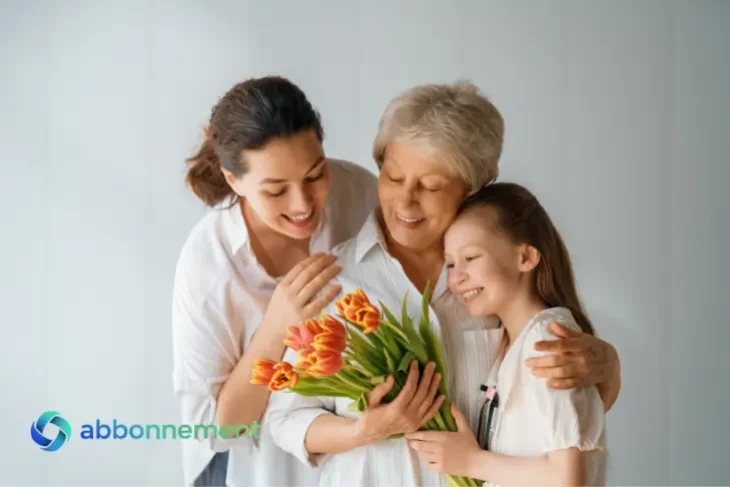 Donna anziana abbracciata da figlia e nipote con fiori, festa della mamma