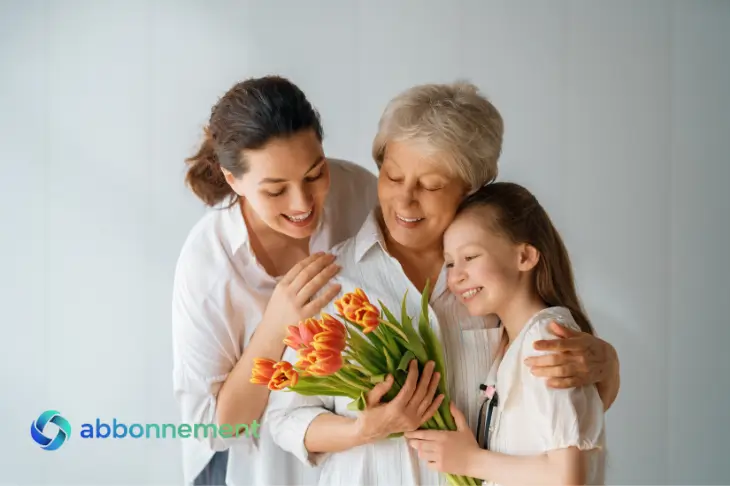 Donna anziana abbracciata da figlia e nipote con fiori, festa della mamma